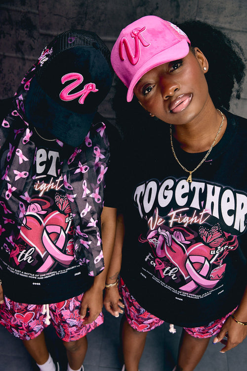 Two people wearing matching outfits with pink and black designs, standing against a dark background.